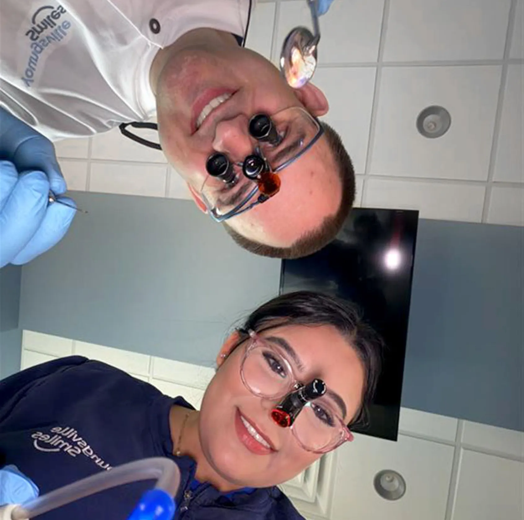 Smiling male and female dentists wearing magnifying glasses and gloves in a dental office.
