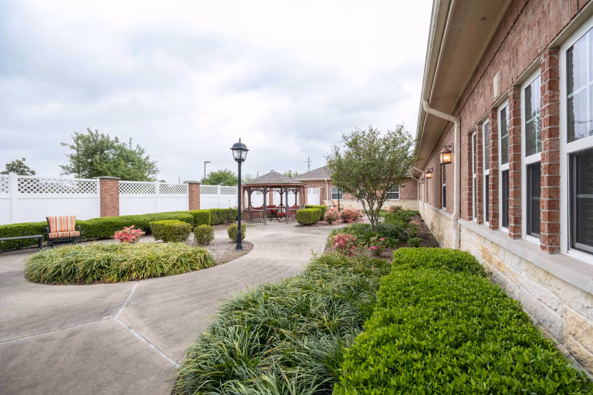 A landscaped courtyard with greenery, a winding pathway, a gazebo, and a lamppost