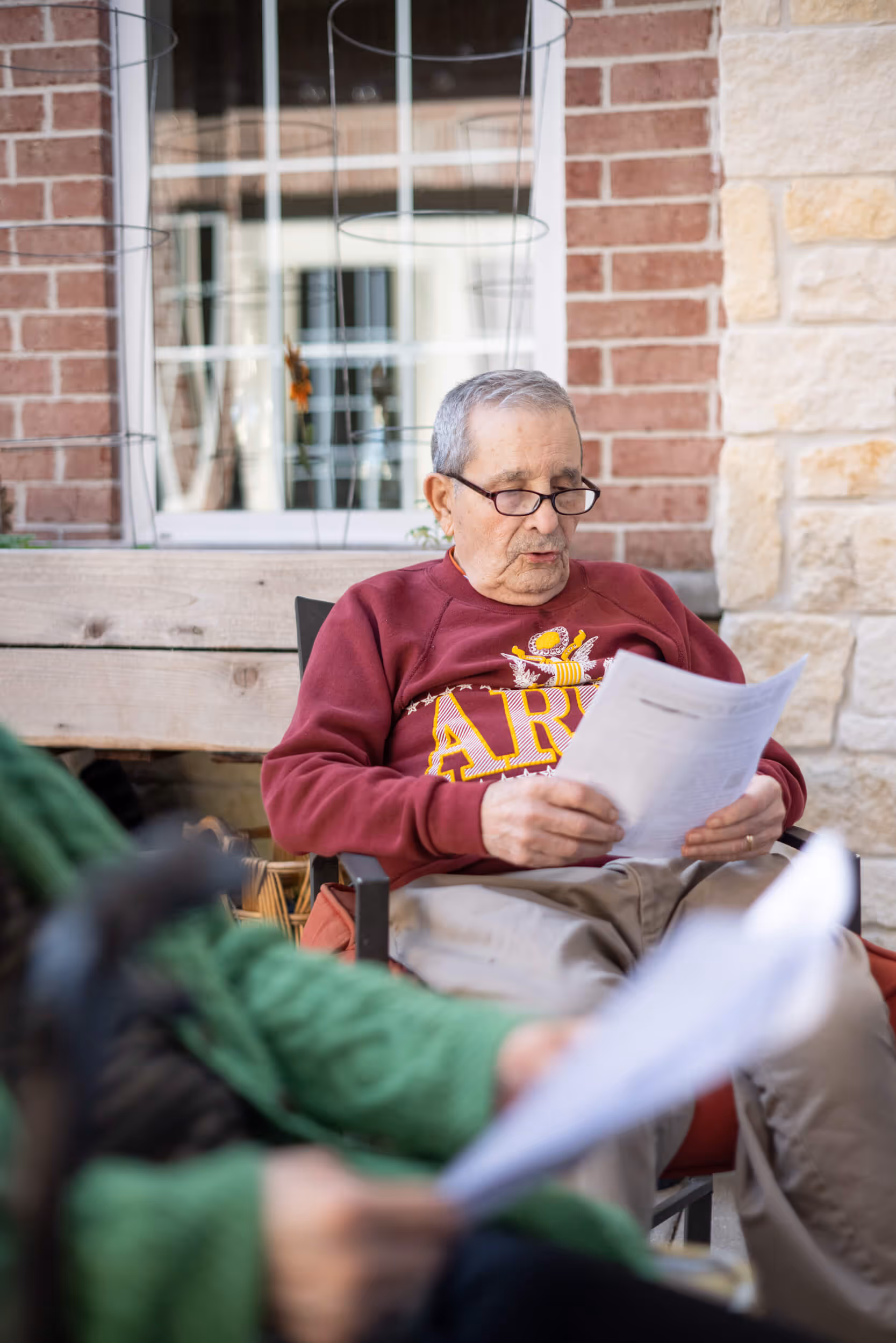 senior man in a red sweater reads a document outdoors