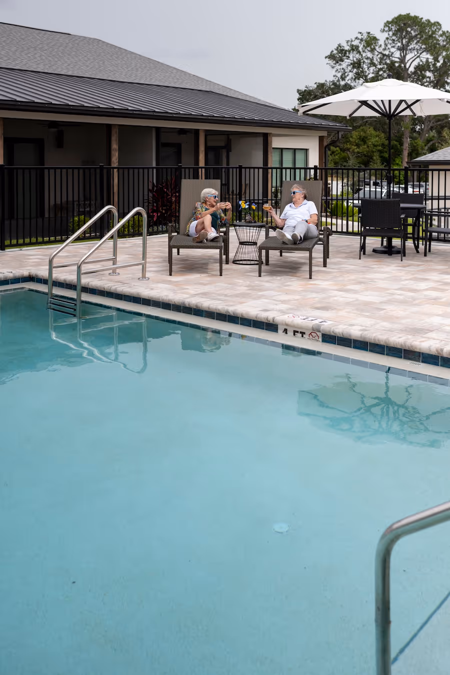 Two senior residents relaxing on lounge chairs by the pool