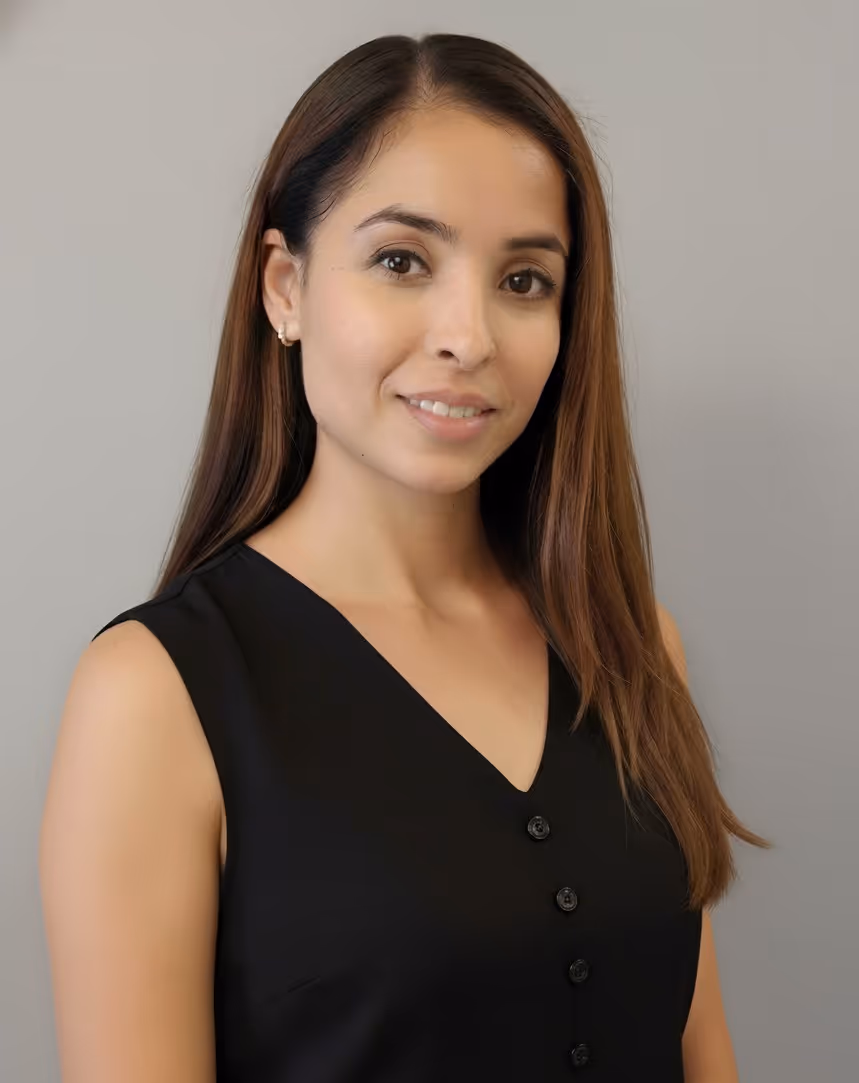 Portrait of a smiling woman with long brown hair wearing a sleeveless black top against a gray background.