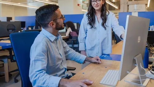 Two professionals discuss in front of an iMac inside Nana Bianca's coworking spaces in Florence, in a modern environment equipped for startups and freelancers.