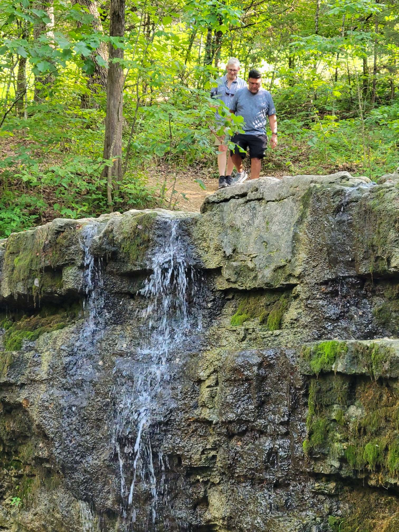 View of the waterfall at the end of the Waterfall Trail, with two hikers at the top.