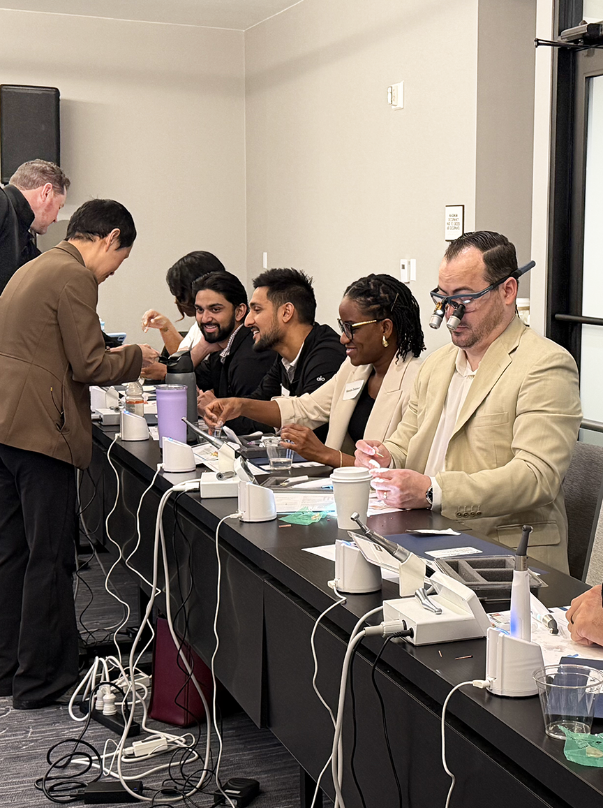 Dentists seated at a long training table during a DDS Academy course