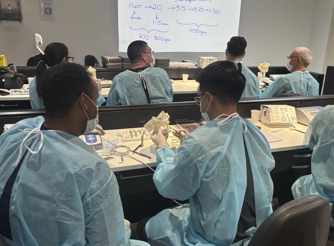 Doctors in gowns practicing implant techniques on jaw models