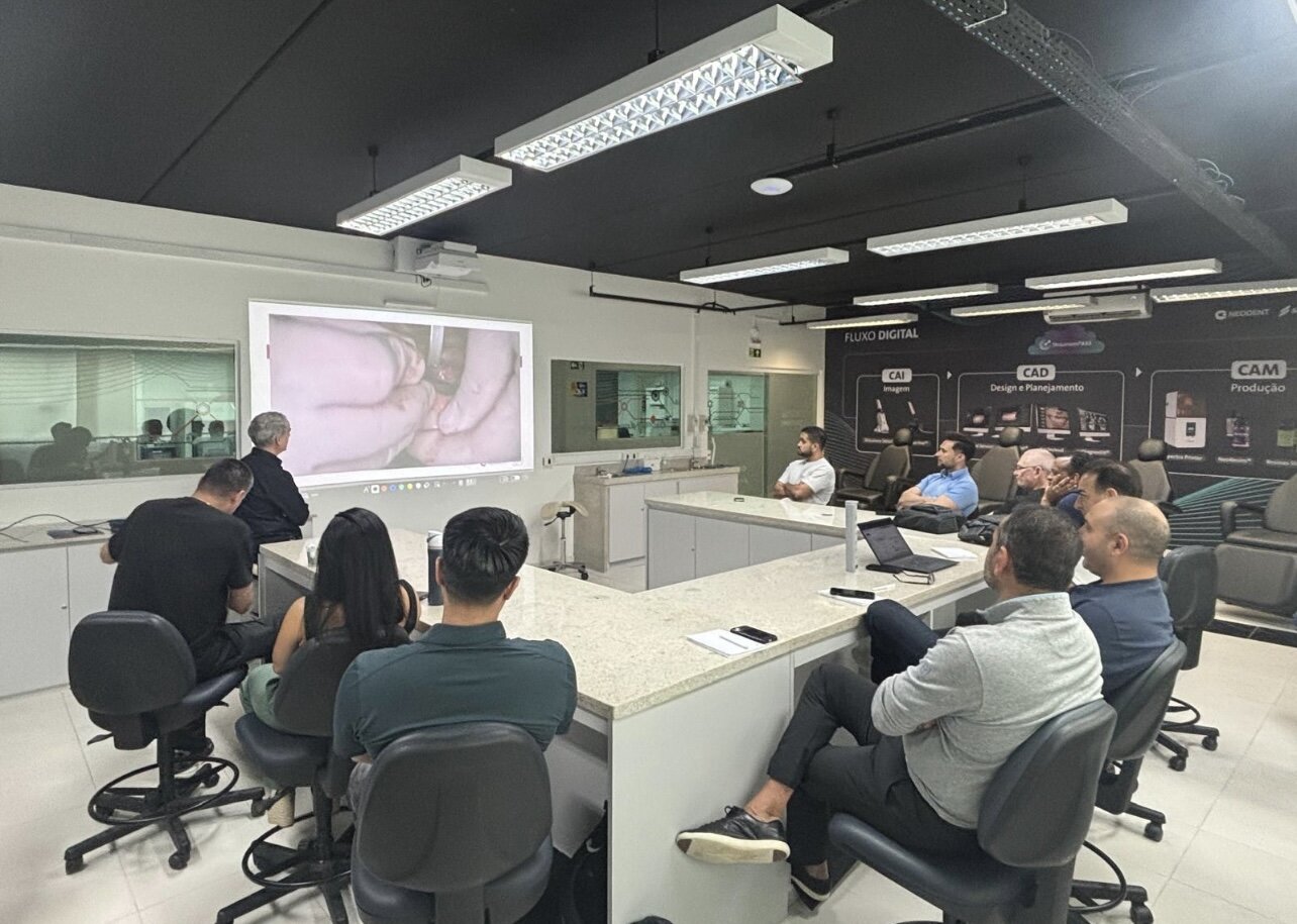 Doctors seated around a training table watching a live clinical demonstration on screen