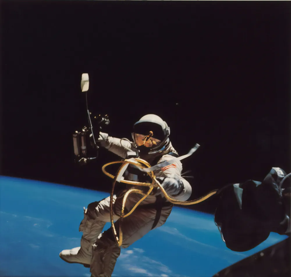 Astronaut in a white spacesuit floating in space with Earth visible below and tether attached.