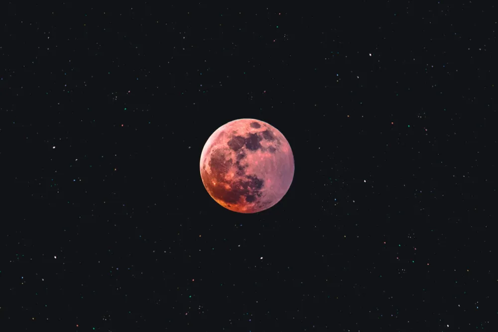 Red-colored full moon surrounded by a starry night sky.