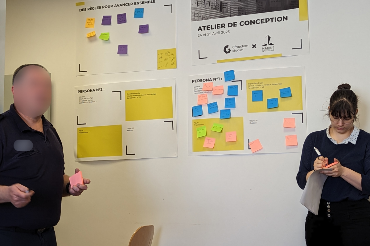 ilana prend des notes pour créer des personae devant des poster et des post-it pour la facilitation d'atelier