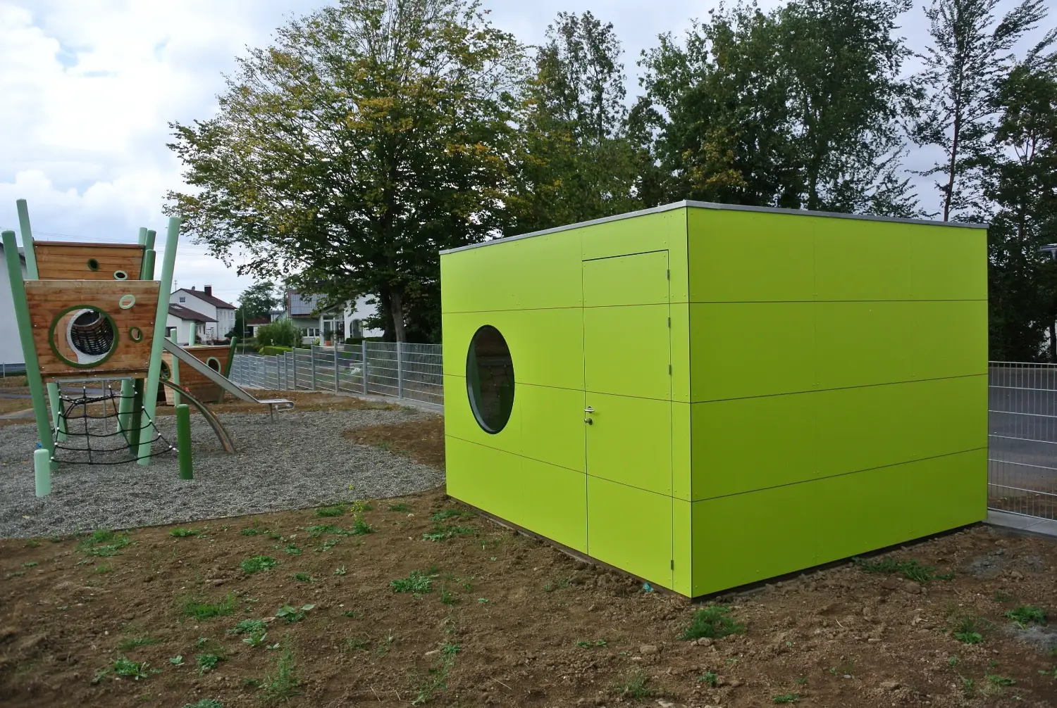 Großes, quietschgrünes Design-Gerätehaus neben einem Spielplatz gelegen, mit Flachdach und rundem Fenster