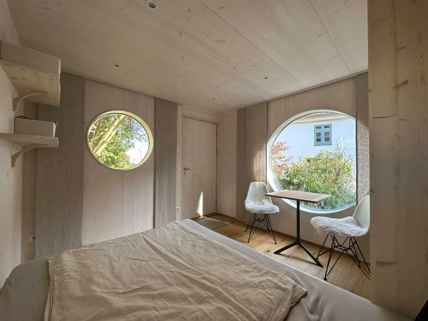 Blick vom Bett auf den gemuetlichen Essbereich mit großen, runden Fenstern im Innenraum eines isolierten Gartenhauses
