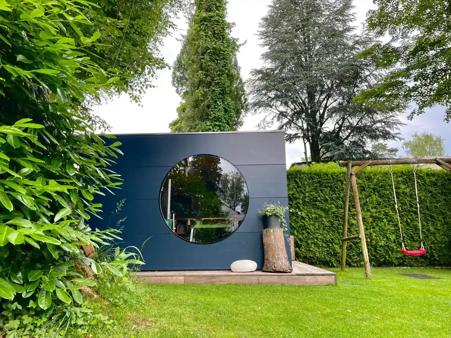 Großes Gartenhaus in Dunkelgrau, dient als Gerätehaus und Werkstatt, mit Holzterrasse, gelegen in einem großen Garten