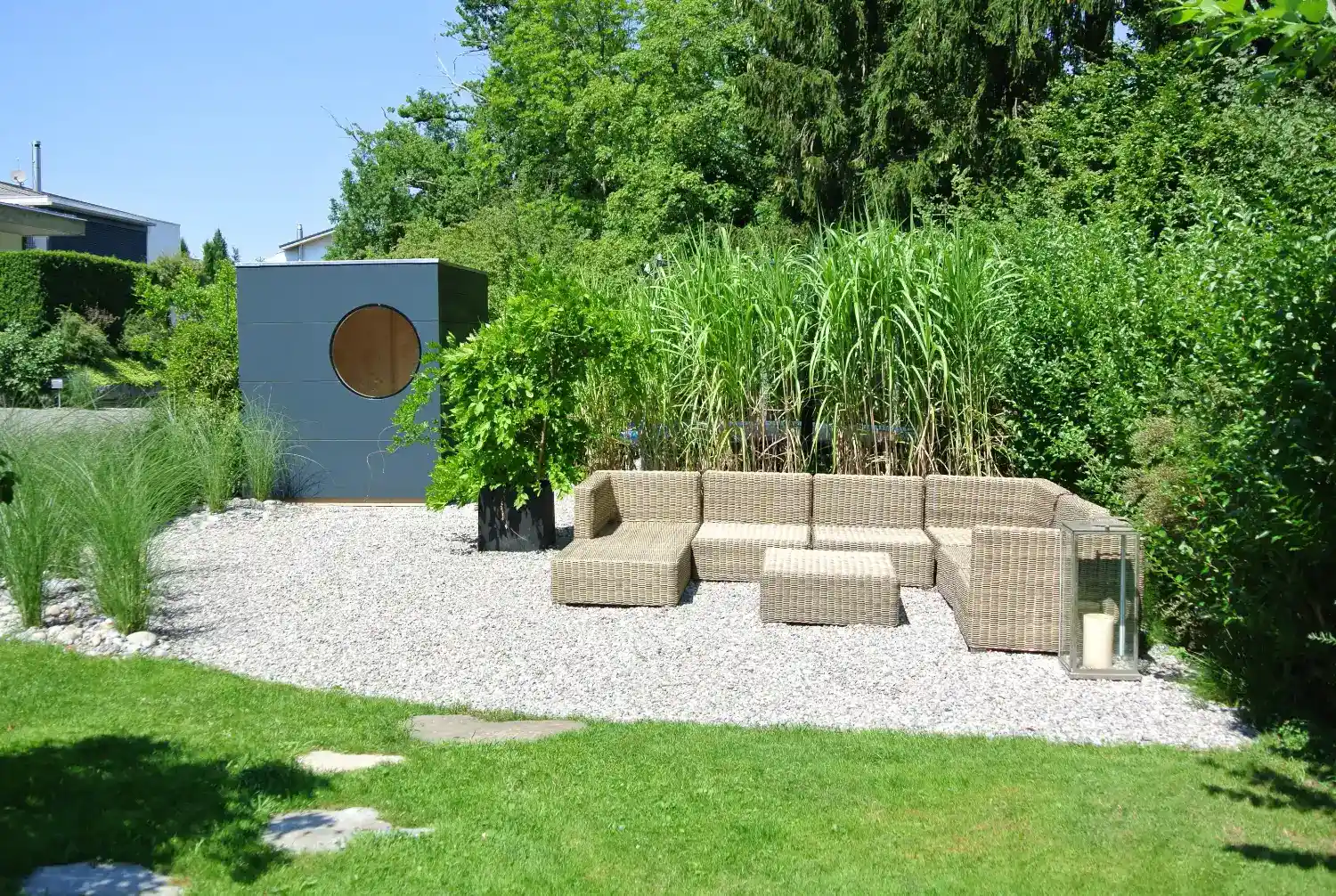 Moderner, neuroaesthetischer Garten mit viel Gruen, Sofalounge, Kiesbett und dunkelgrauem, modernen Gartenhaus Kubus