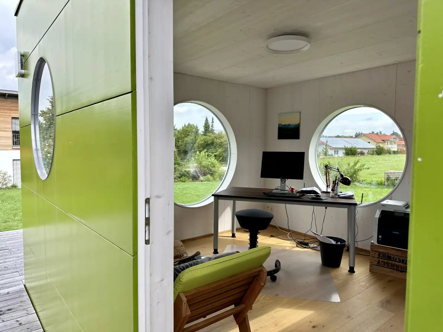 Blick in neuroaesthetisch gestaltetes Buero im Gartenhaus, runde Fenster, Inneneinrichtung passend zur gruenen Fassade