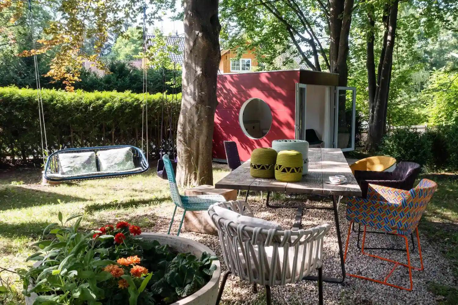 Gartenhaus Ausstellung mit rotem Garten Kubus, Blumen und Straeuchern, Design-Outdoormoebeln, alten Baeumen und Schaukel