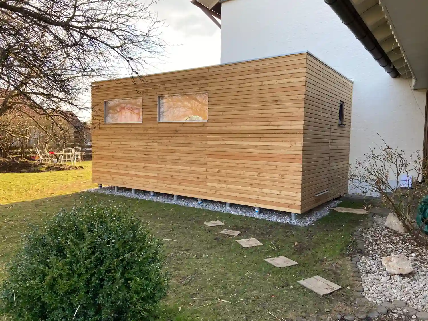 Modernes Design Gartenhaus mit Flachdach und Lärche Rhombus Fassade naturbelassen, dahinter weißes Haupthaus