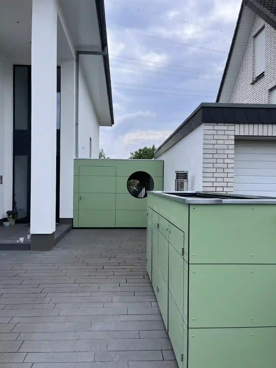 Modernes Gartenhaus mit passendem Muelltonnenhaus zwischen Wohnhäusern gebaut, beide mit gruener HPL Fassade
