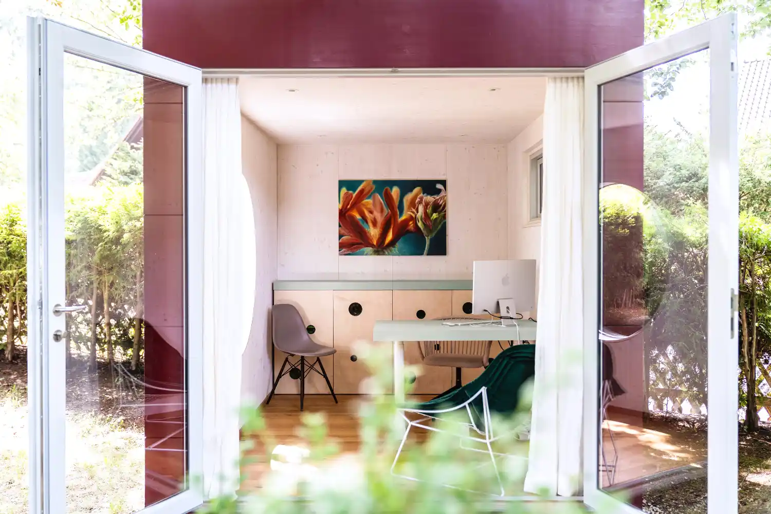 Blick durch offene Doppelflügeltür in ein Homeoffice im Gartenhaus mit Schreibtisch, Regal, Stühlen und Wandbild