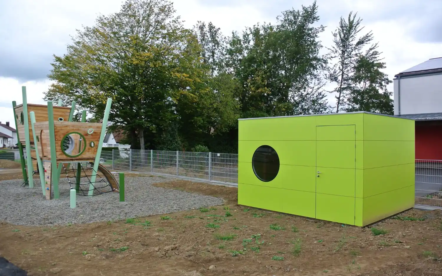 Knallgrün gestrichenes Gartengerätehaus in modernem Design mit Rundfenster und Flachdach auf Spielplatz neben Kletterturm