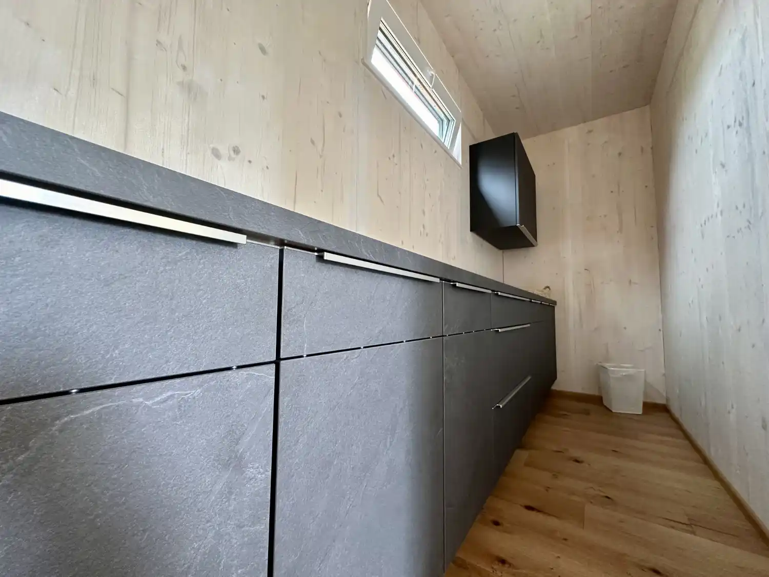 Blick in kleinen, abgetrennten Raum aus Holz mit grauen Küchenmöbeln als extra Küche eines Gartenbüros