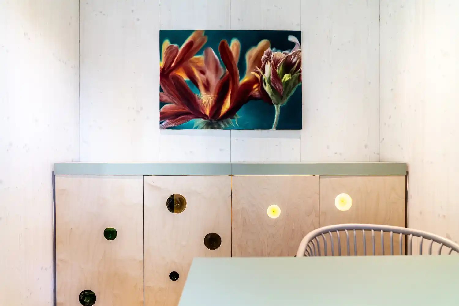 Detailblick in Gartenbüro mit weiß lasierten Holzwänden, Schrank mit runden Glaselementen, Bild und Schreibtisch