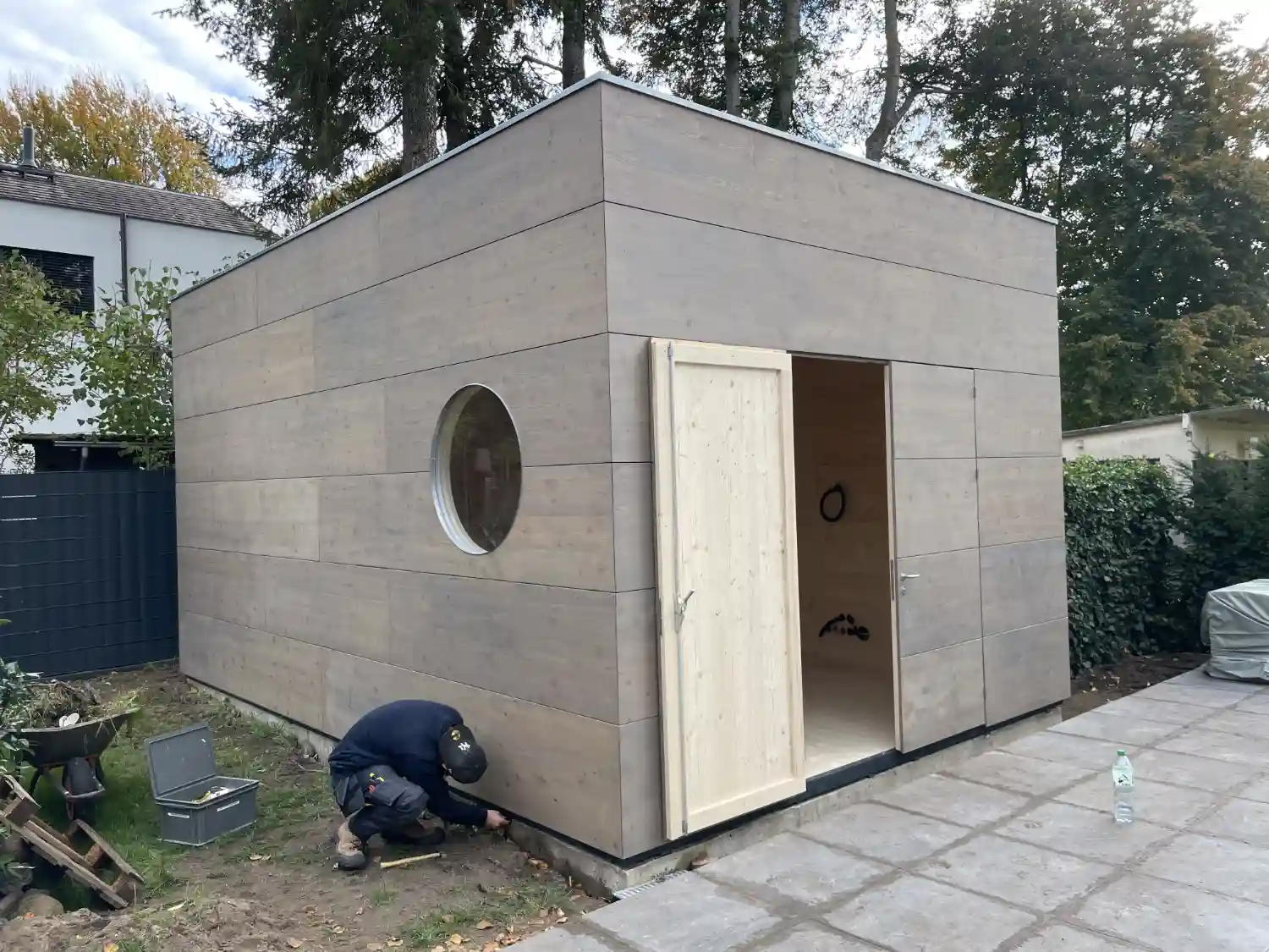 Grosses Gartenhaus mit vergrauter Laerche-Fassade, Flachdach, Rundfenster und Doppelfluegeltuer, mit Golf-Simulator fuer Golftraining