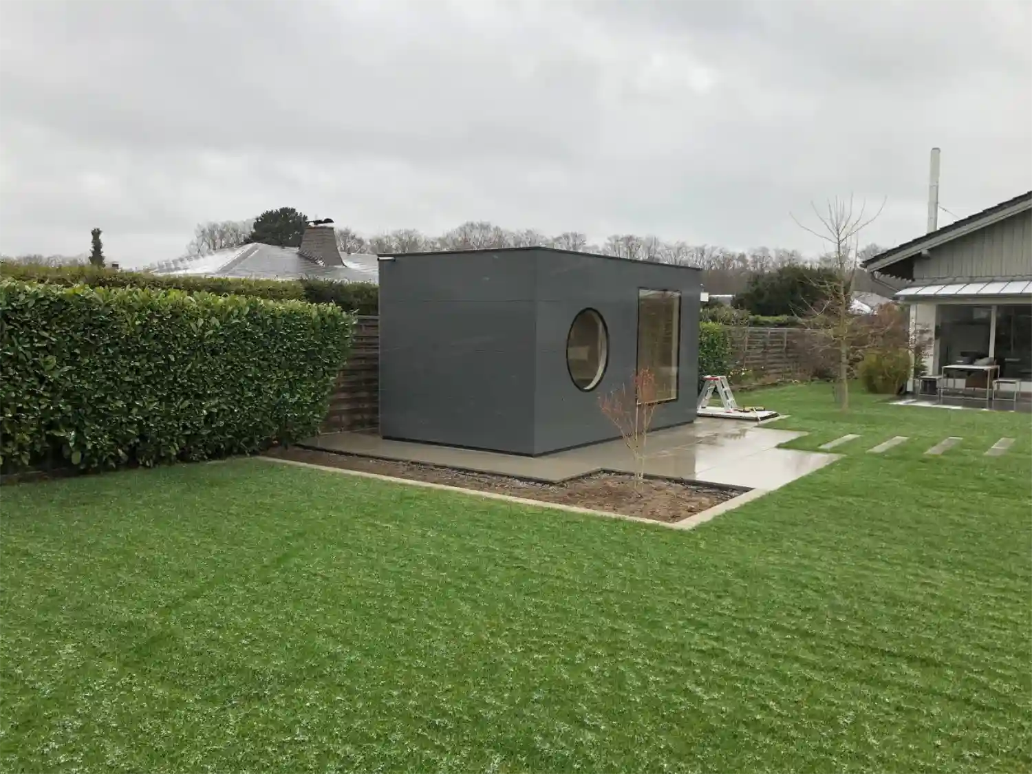 Design-Gartensauna im grossen, regnerischen Garten mit lackierter, grauer Holzfassade als Schutz vor Naesse