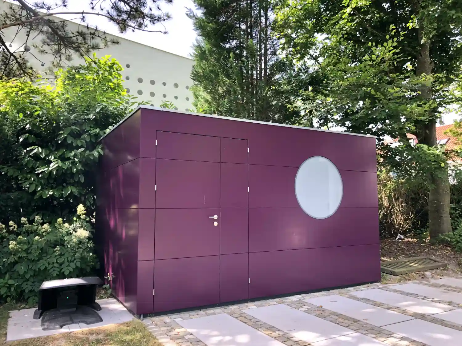 Design-Gartengeraetehaus mit auffaellig lila gestrichener Holzfassade als Blickfang zwischen eintoenigen Haeusern