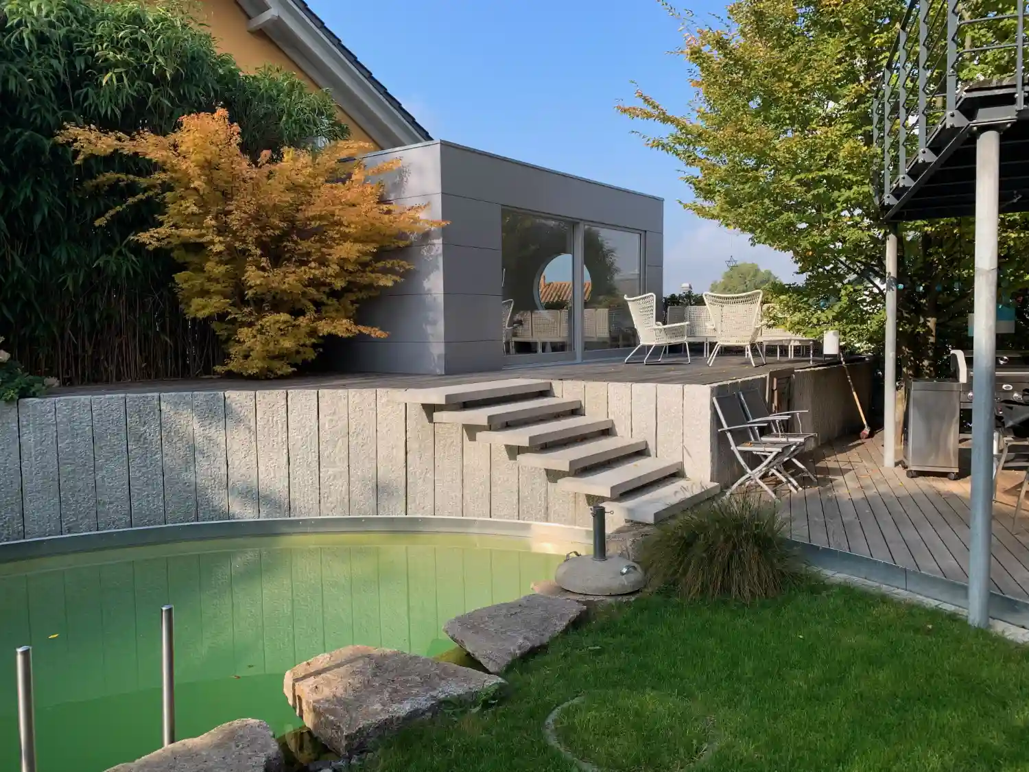 Modernes, hochwertiges Poolhaus erhoeht auf Terrasse neben Teich, Holzfassade in modernem grau