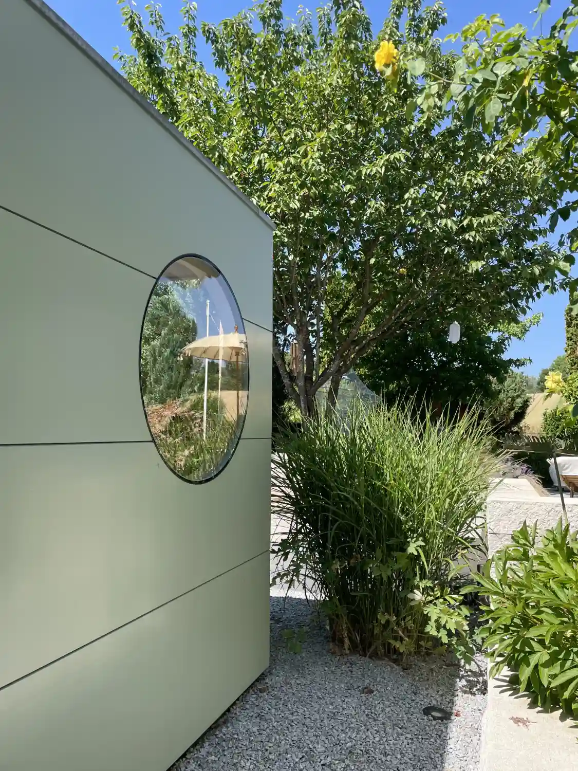 Detailblick auf blassgruen gestrichene Holzfassade aus Fichte-Verbundplatte eines modernen Gartenhauses mit Rundfenster