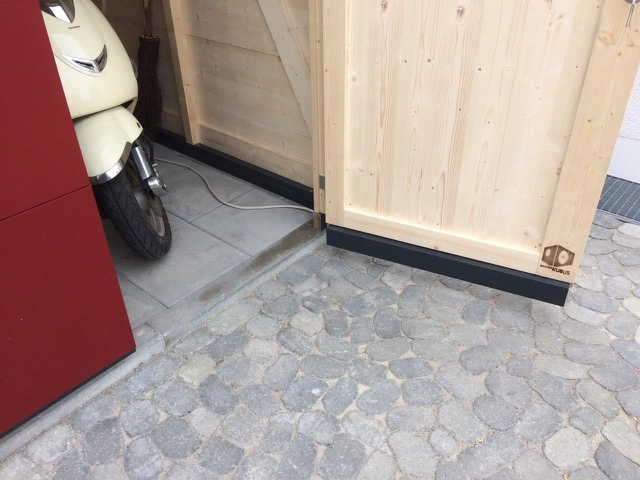Detailblick auf den ausgeklinkten Bodenrahmen bei der Tuer eines Garten Kubus Gartenhauses mit roter Fassade