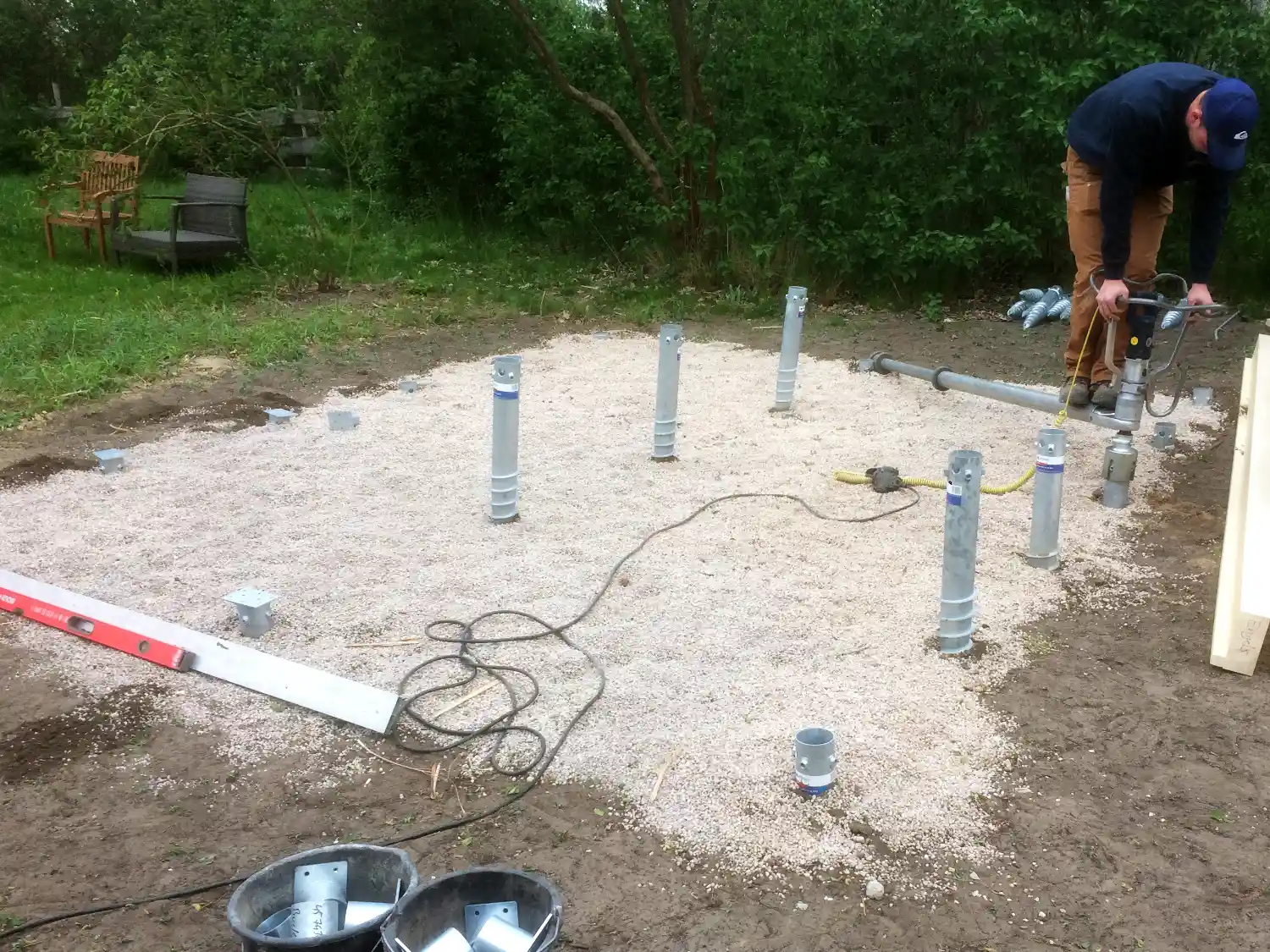 Baustelle im Garten, gekieste Flaeche in die ein Monteur Schraubfundamente eindreht als Fundament fuer ein Gartenhaus