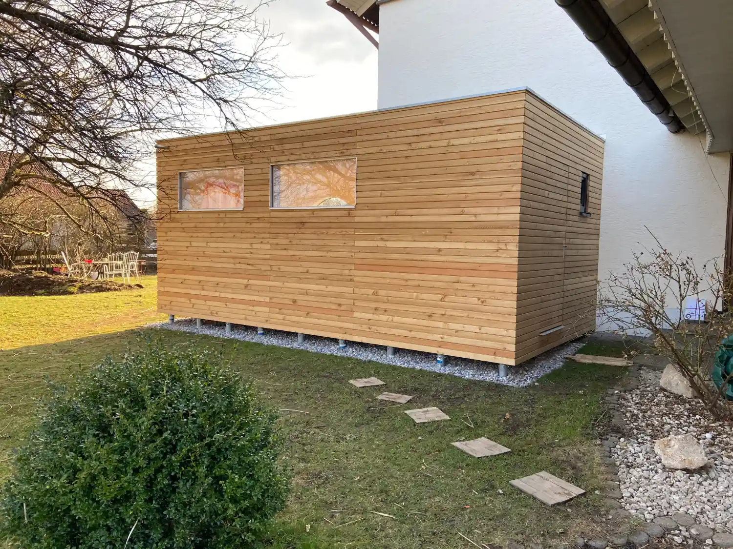 Blick auf einen Garten Kubus als Hausanbau mit Fassade aus Laerche-Rhombus und auf Schraubfundamenten montiert