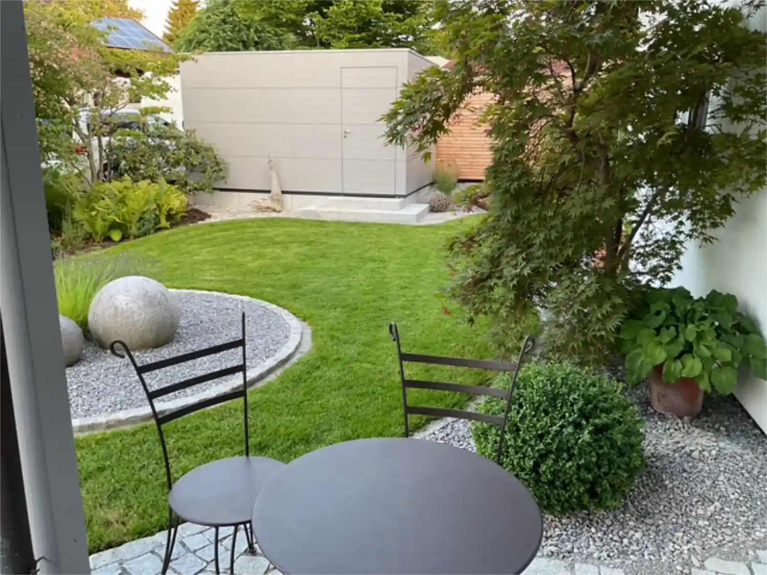 Stilvoller, moderner Garten mit geschwungenen Kanten, Pflanzen und modernem Gartenhaus in grau auf Plattenbelag