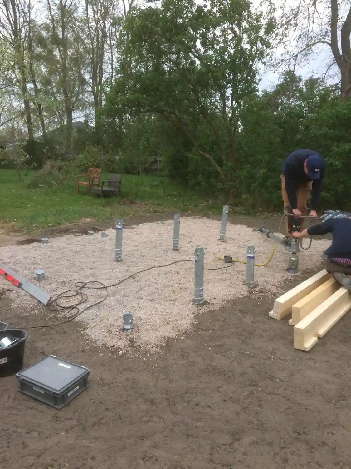 Zwei Mitarbeiter drehen Krinner-Schraubfundamente an den geplanten Positionen für ein Gartenhaus ein