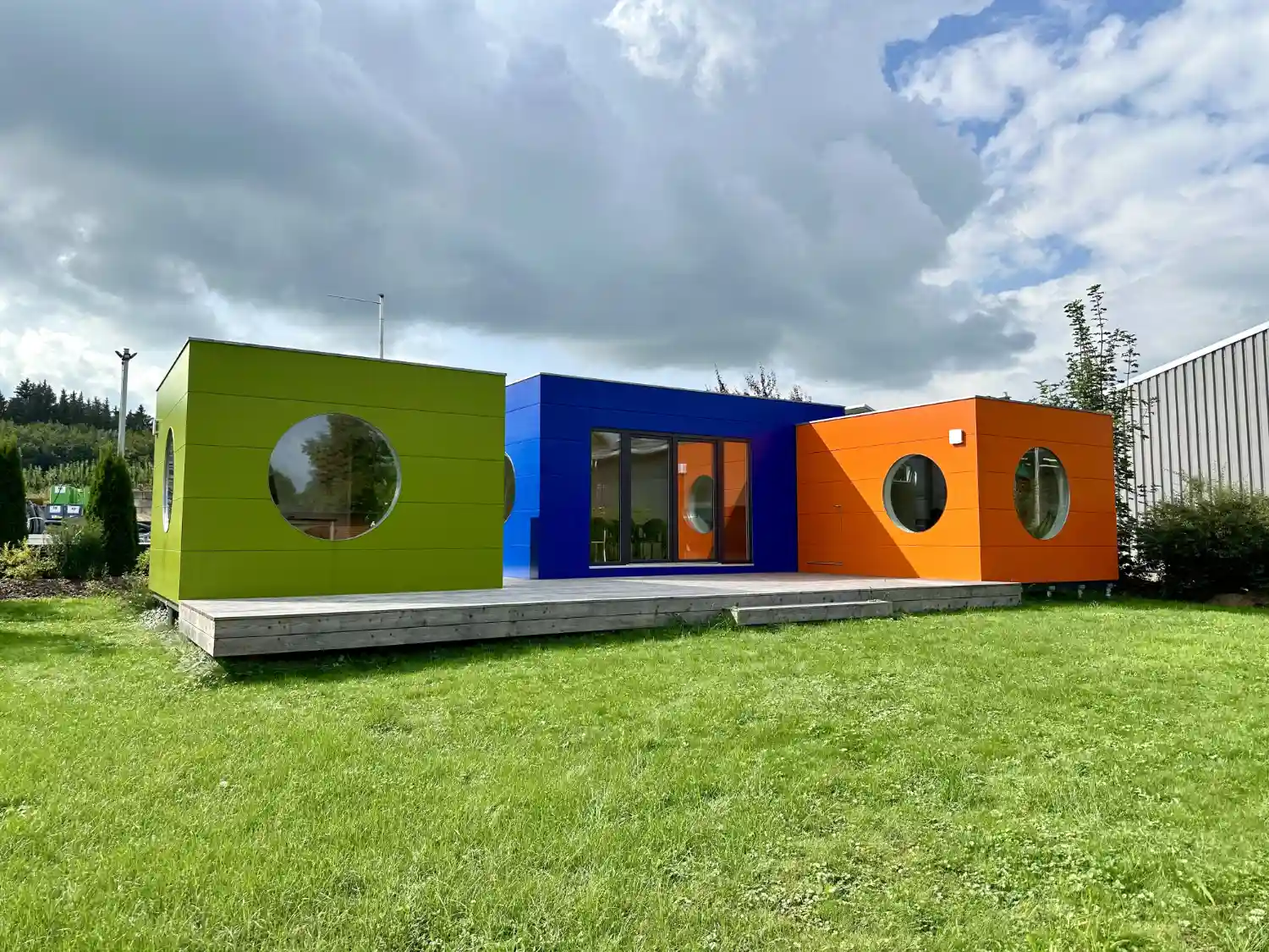 Drei Office Kuben in Grün, Blau und Orange als Gartenbüros und Meetingraum auf Schraubfundamenten mit gemeinsamer Terrasse
