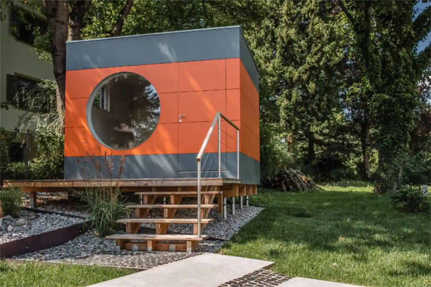 Gartenbüro mit grauer und orangener Holzfassade auf unterschiedlich langen Schraubfundamenten in unebenem Gelände