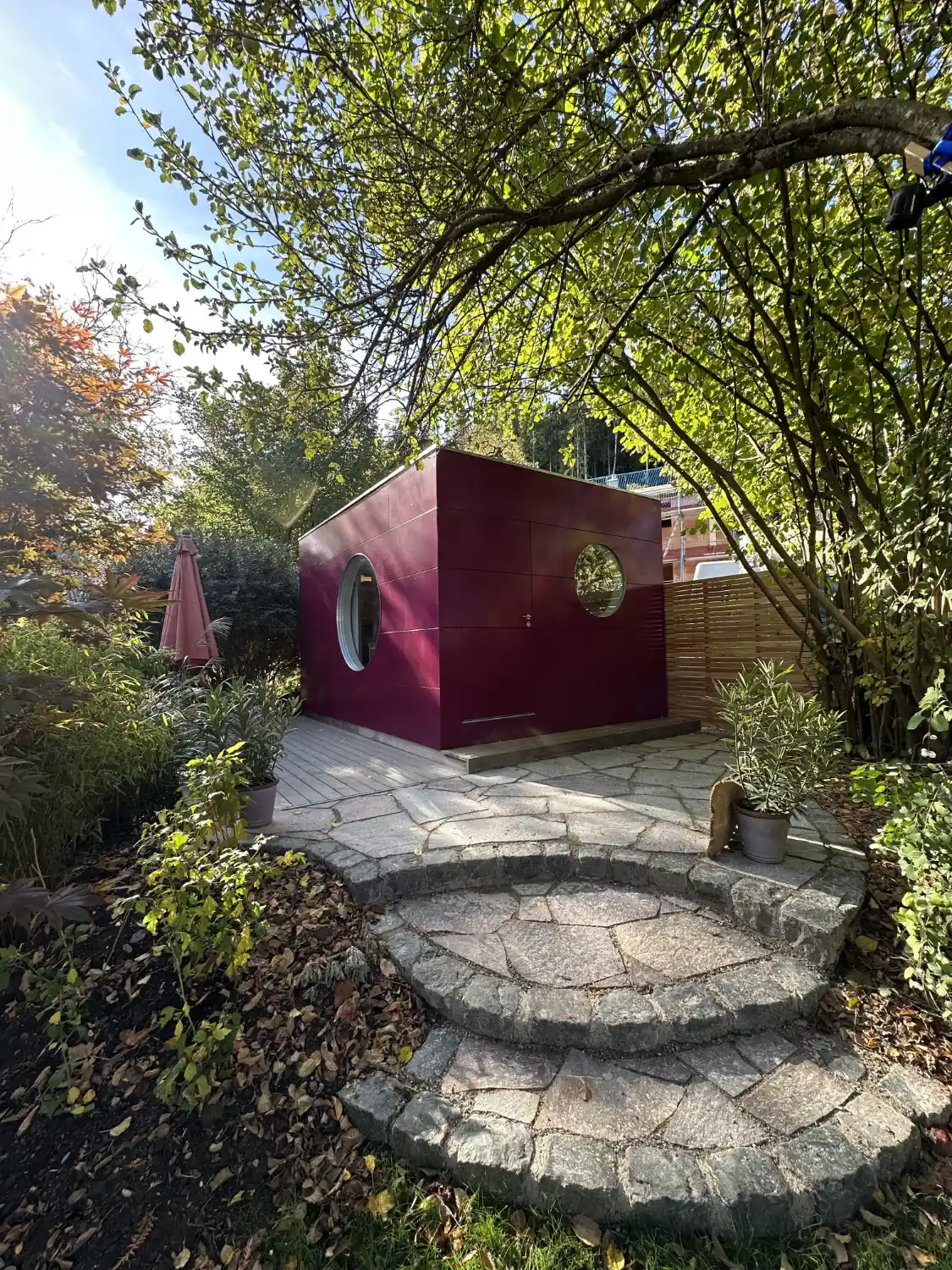 Isoliertes Gartenhaus mit pinker Holzfassade, runden Fenstern und steinernen Stufen im Garten
