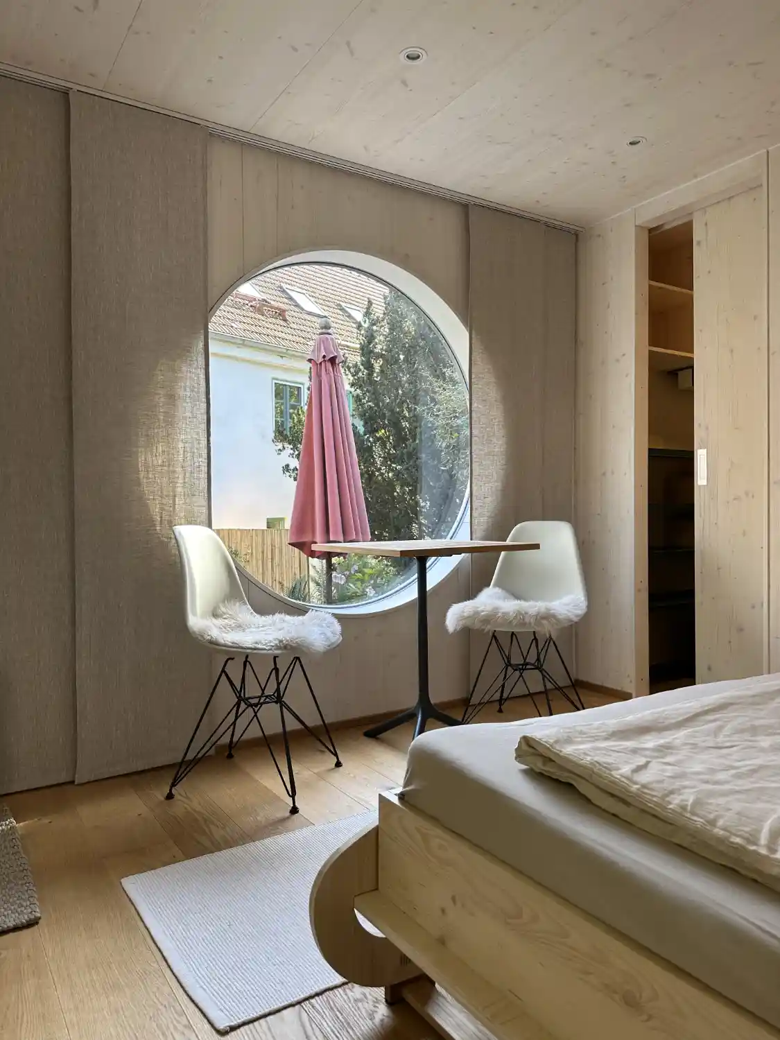 Innenraum des Tiny Houses mit weiß lasierten Fichtenwänden, Eichenparkett, Holzmöbeln und rundem Fenster