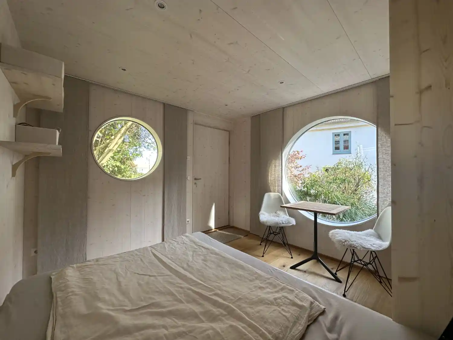 Blick vom großen Klappbett in den hellen Wohnbereich des Tiny Houses mit Esstisch, zwei Stühlen und Deckenspots