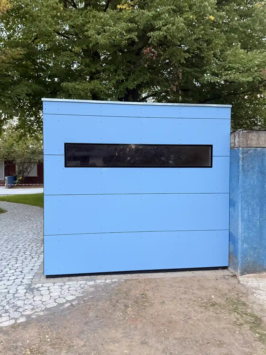 Blick auf Seite eines Gartenhauses in Kubusform mit HPL-Fassadenplatten in Blau und schmalem Oberlichtfenster