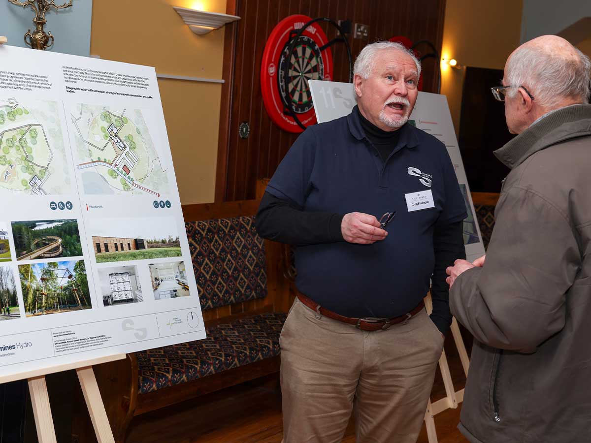 Two elderly men talking near presentation boards with maps and photos in a cozy room.
