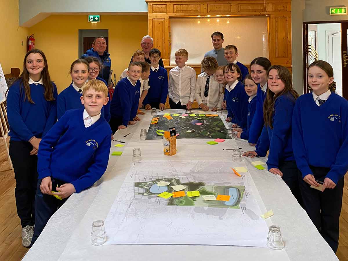 Group of schoolchildren in blue uniforms standing around a table with maps and sticky notes.