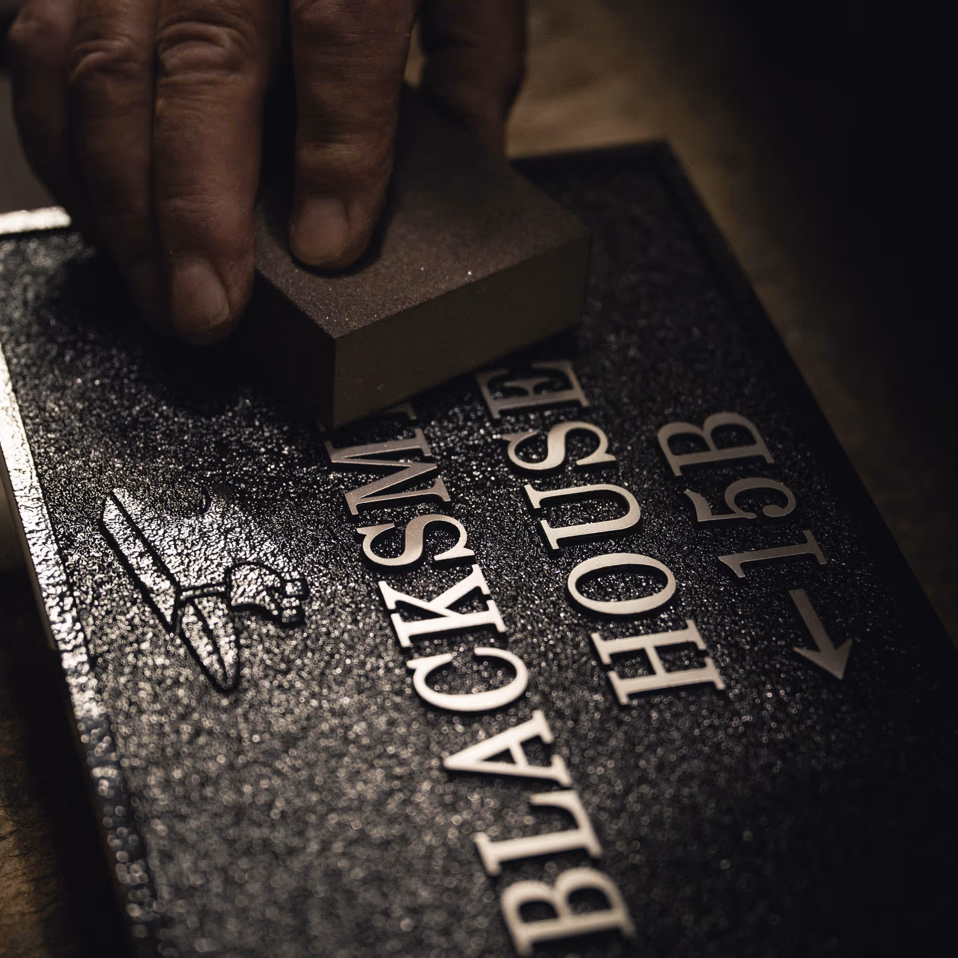 Craftsman linishing raised lettering on bespoke aluminium house sign to reveal polished silver finish.