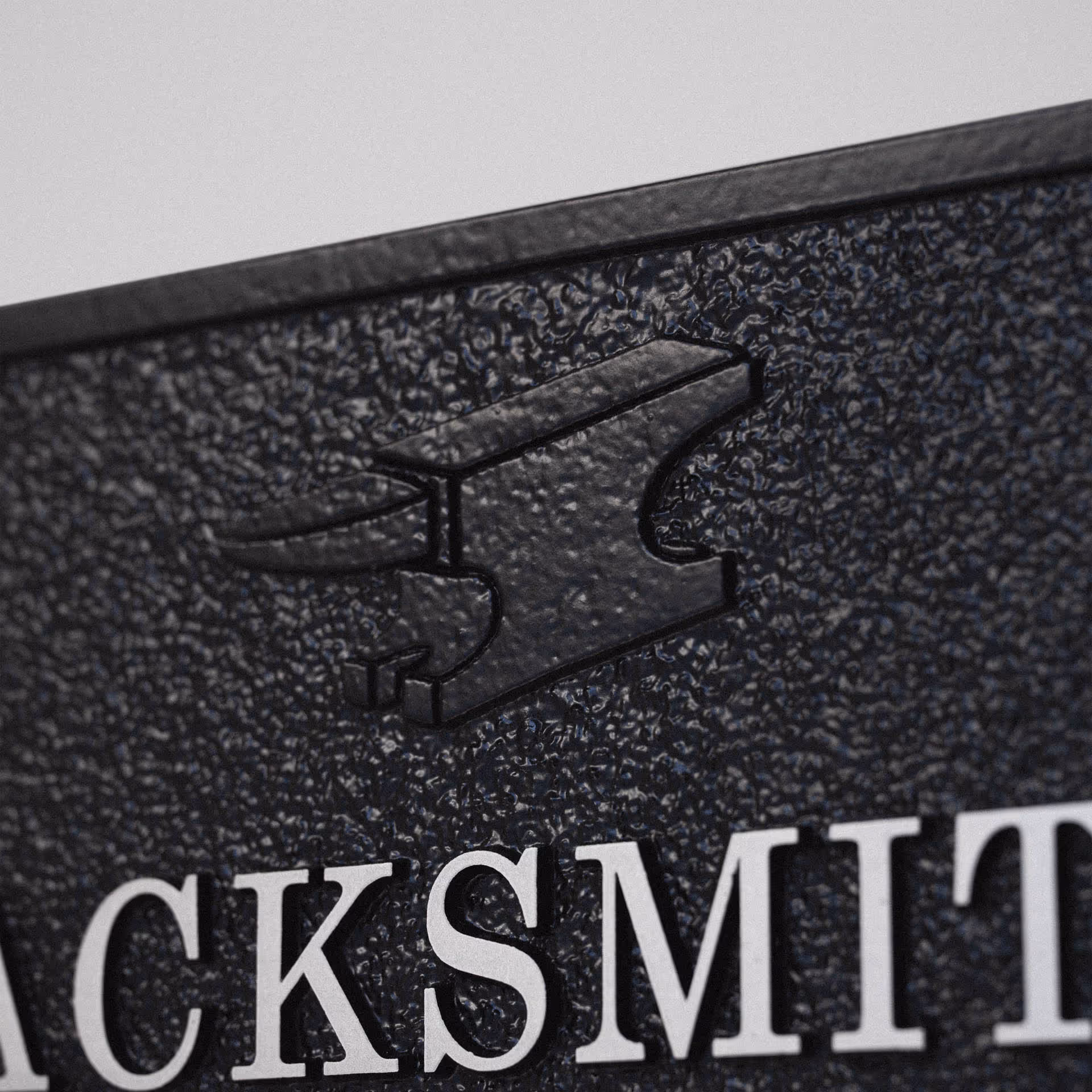 Detail of anvil motif in relief on custom cast aluminium house sign.