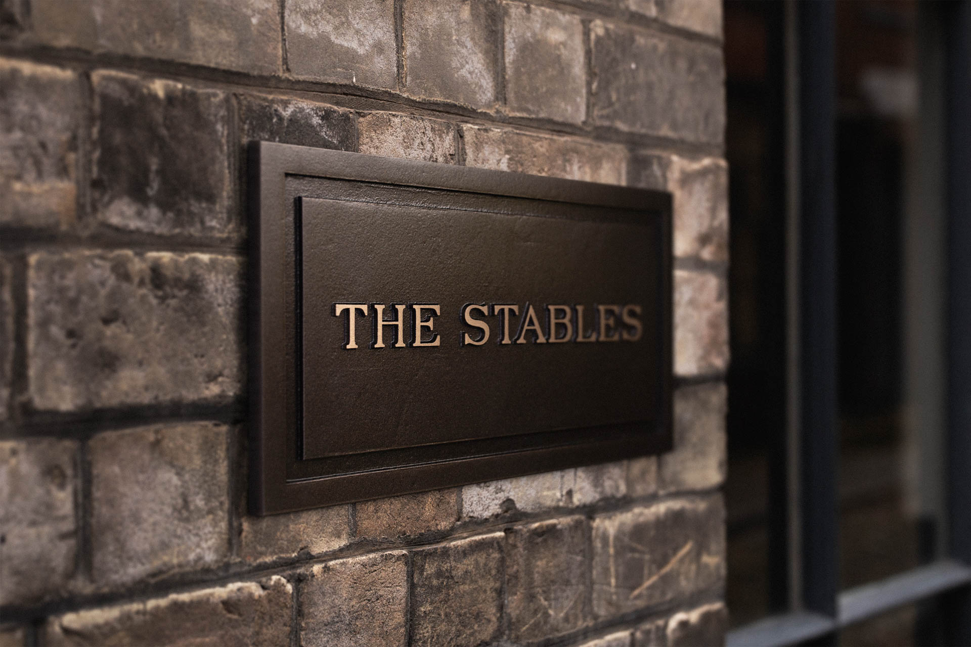 Bespoke luxury cast bronze house sign reading ‘The Stables’, handcrafted and powder-coated with bronze metal powder for a premium, durable plaque finish.
