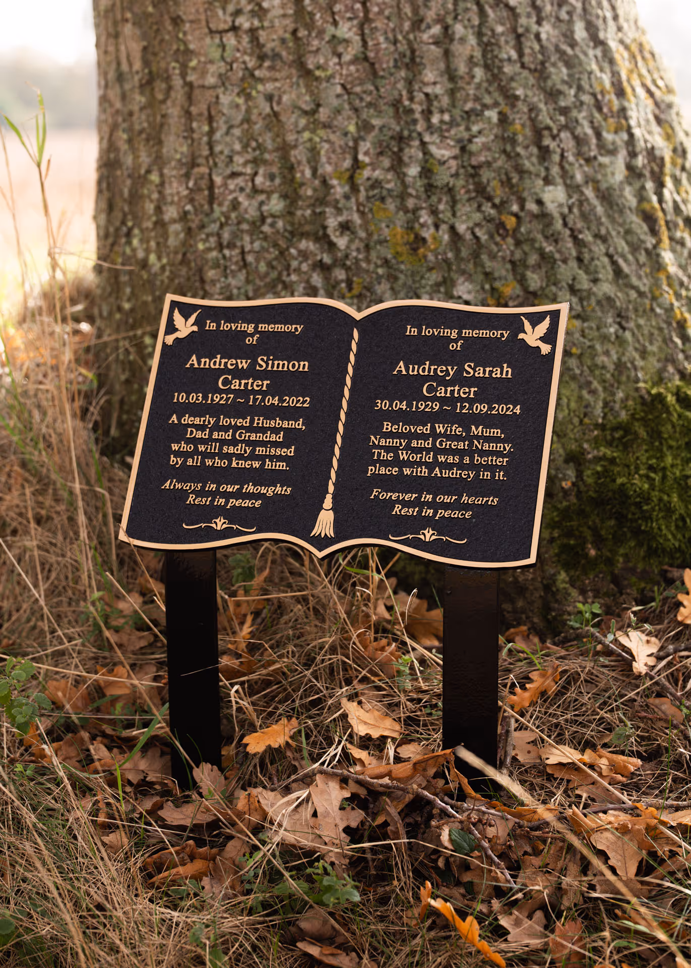 Bronze memorial plaque shaped like an open book, mounted on twin ground stakes for outdoor memorial use.