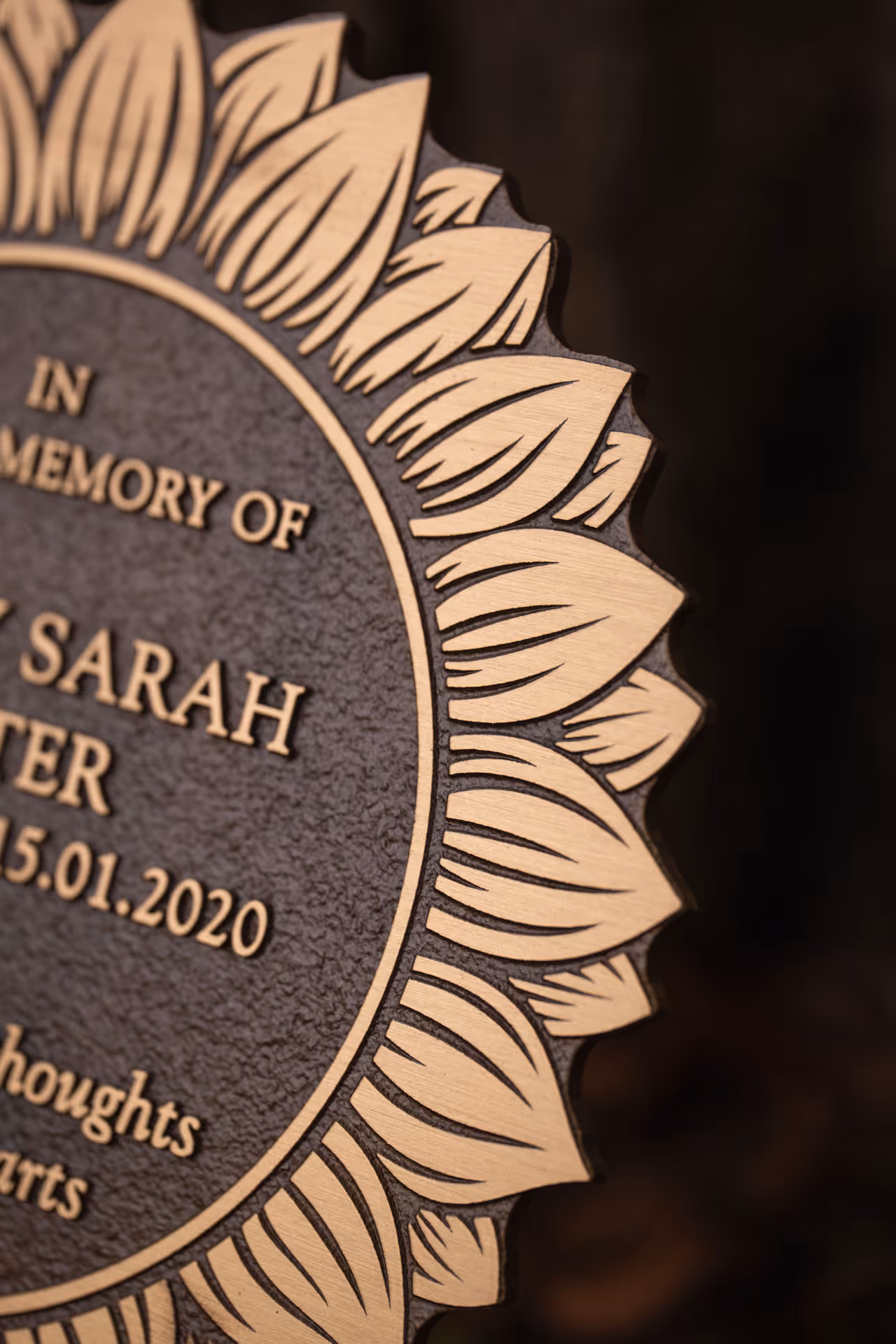 Detail of cast bronze sunflower memorial plaque showing patina and raised design.