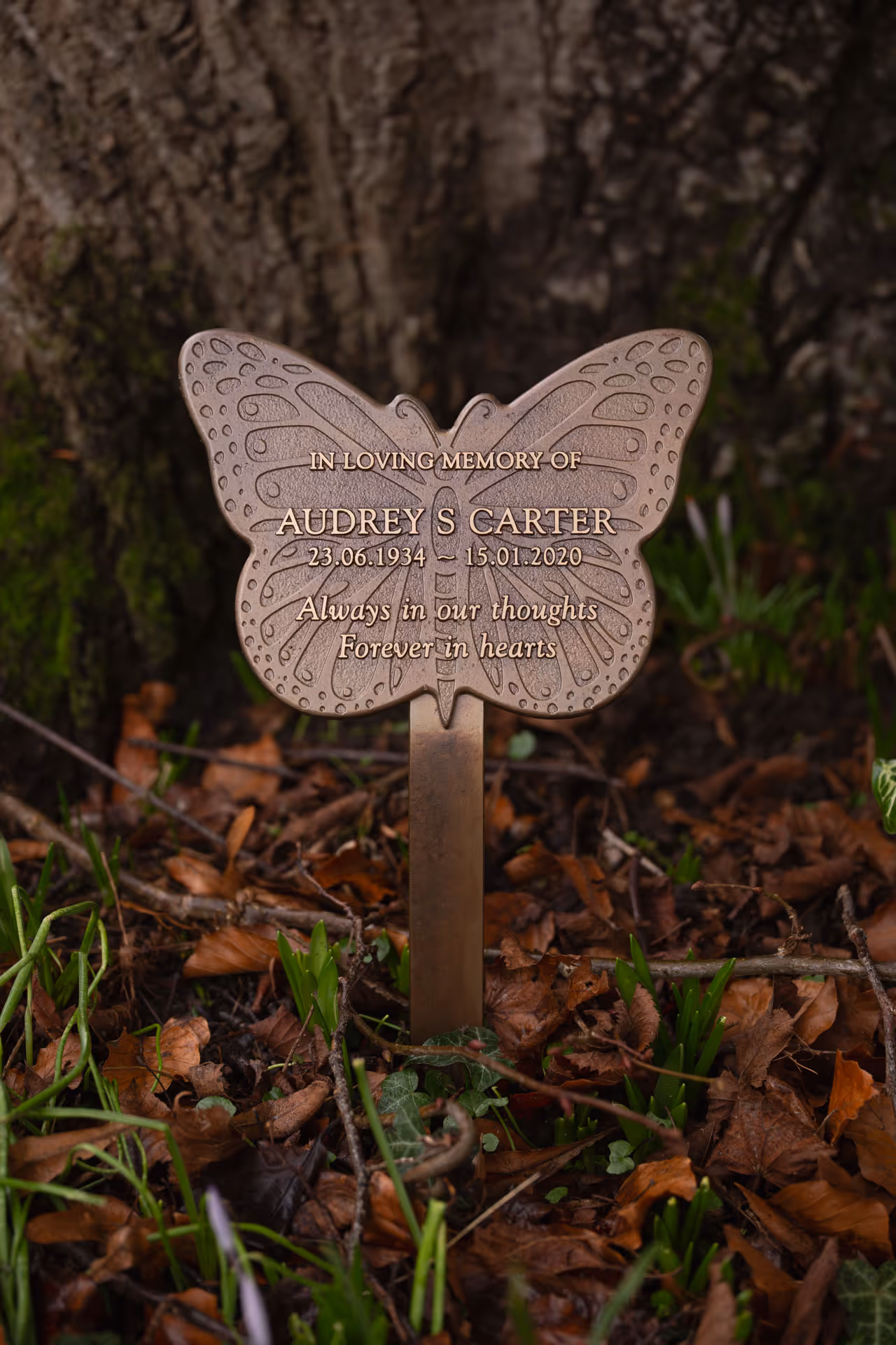 Angled view of a cast butterfly memorial plaque with raised text on a ground stake.
