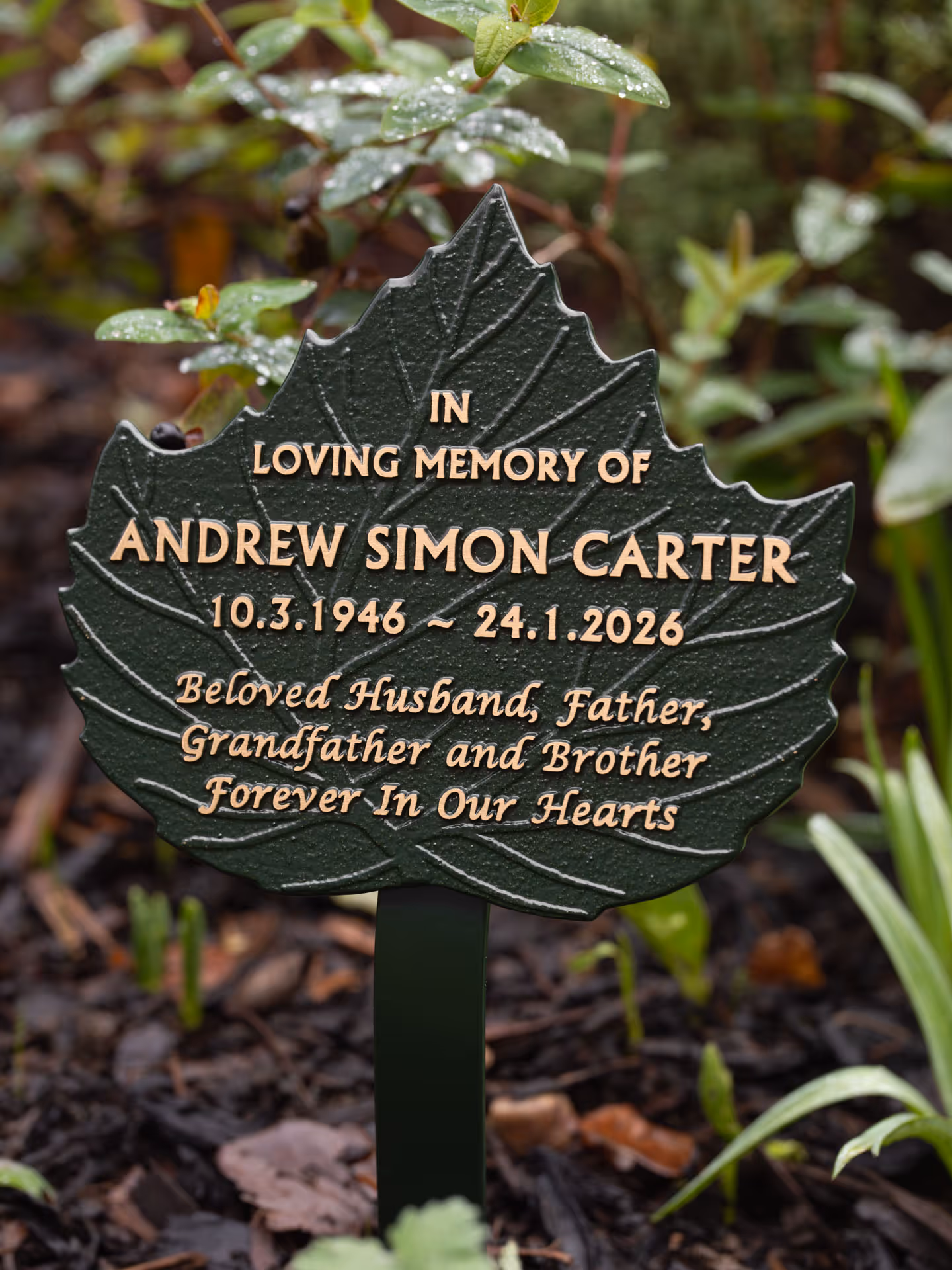 Angled view of a green cast leaf memorial plaque with raised text on a ground stake.